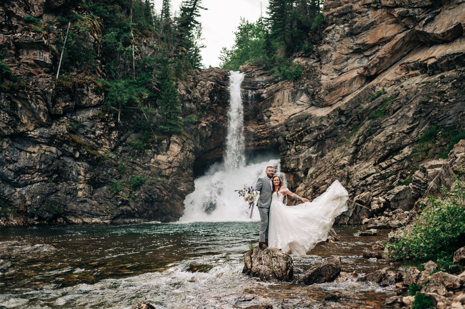 A panoramic view of a cascading waterfall flowing down rocky cliffs surrounded by lush green forest.