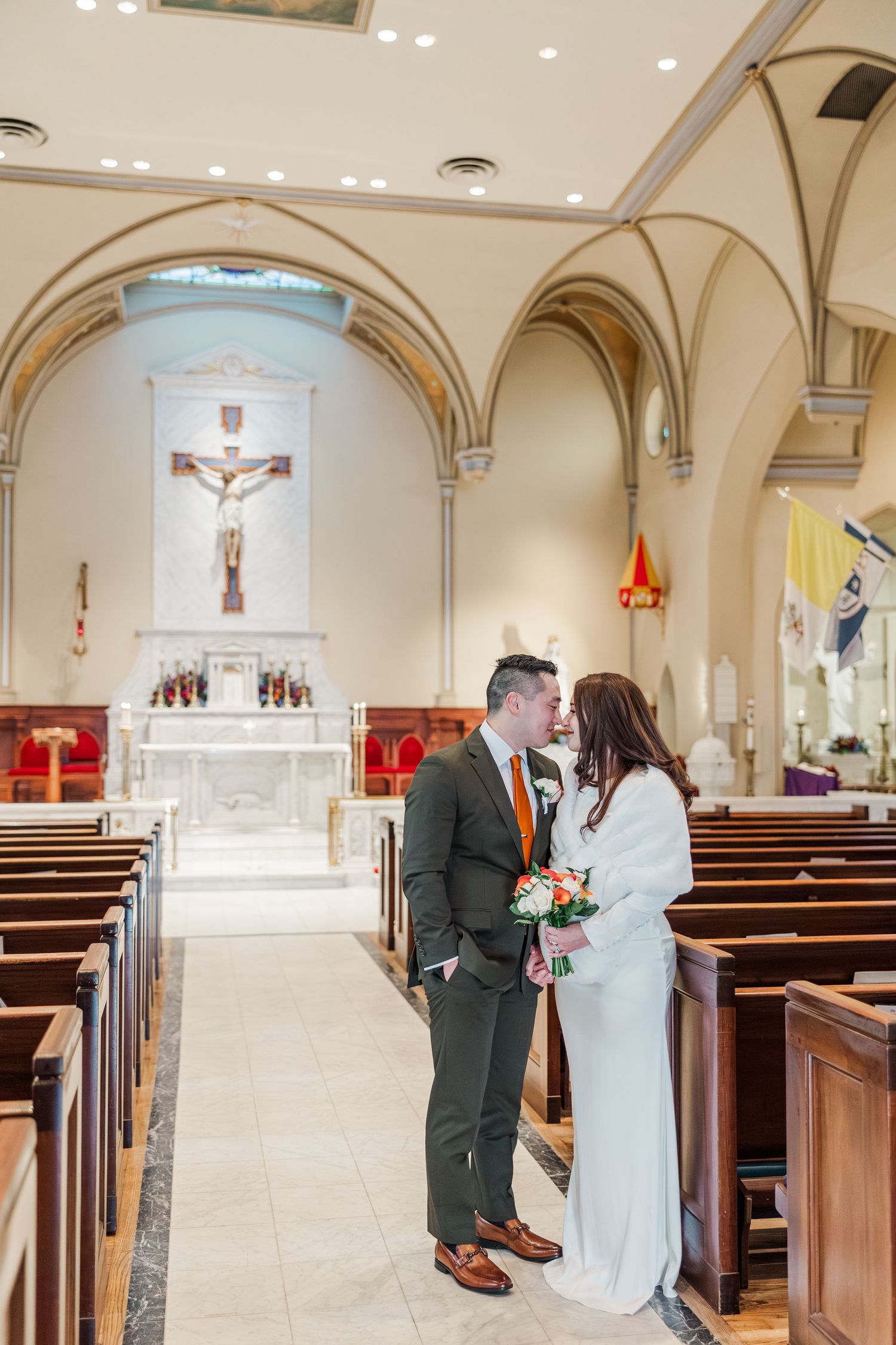 A couple shares an intimate moment in a Catholic church interior with arched ceilings and wooden pews.