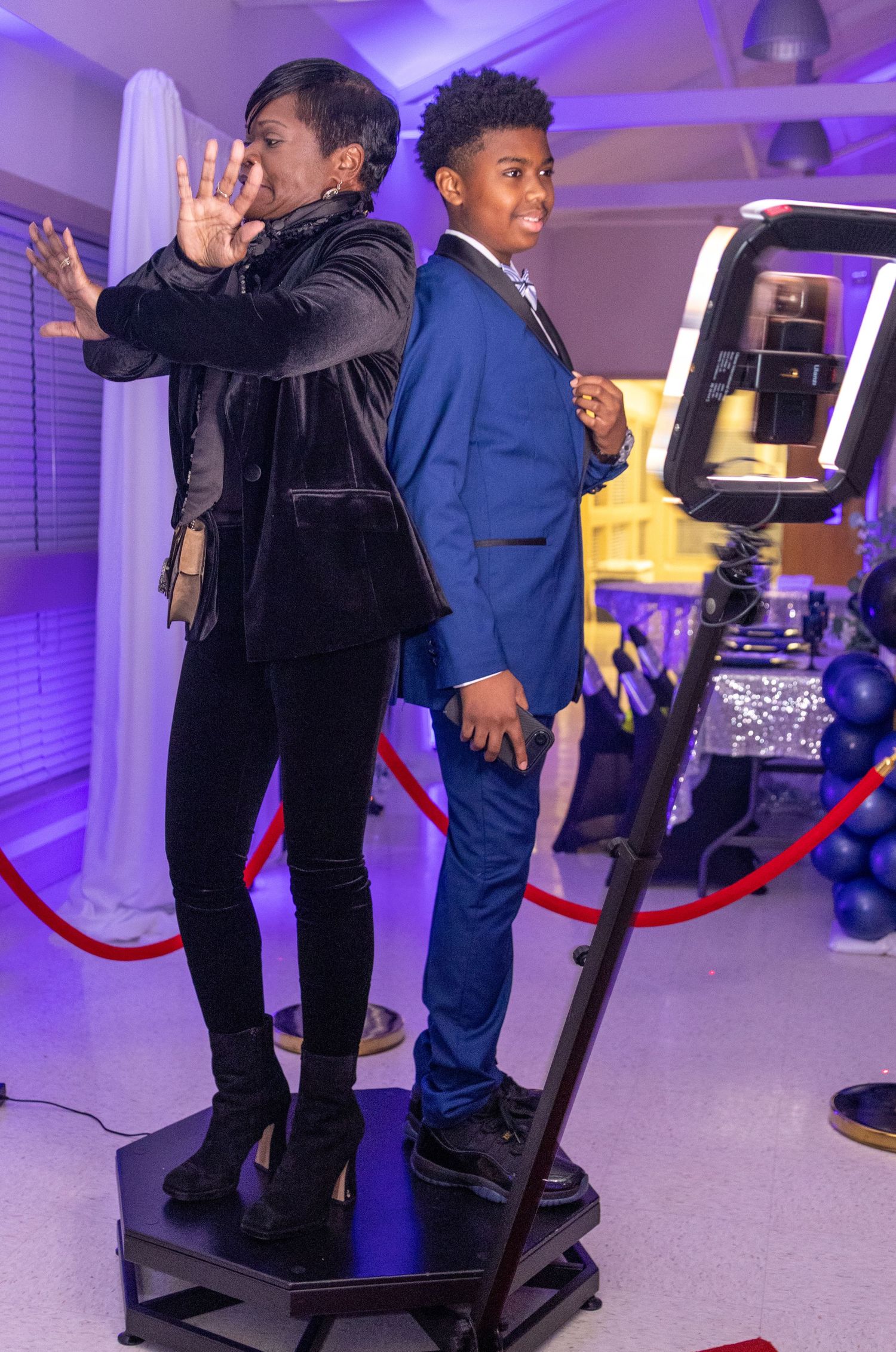 Two people playing an arcade game on a virtual reality platform with purple lighting and red ropes in the background.