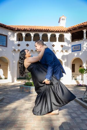 A couple shares a romantic dip pose in a Spanish-style courtyard, woman in black gown, man in navy suit.