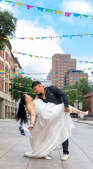 Couple sharing a romantic dip dance pose on a colorful street decorated with festive bunting flags, bride in white gown.