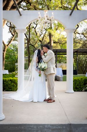 Bride and groom share first kiss under elegant white pergola with chandelier at outdoor garden wedding ceremony.