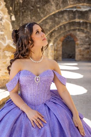 Young woman in a sparkling lavender off-shoulder ball gown with pearl necklace at a quinceañera.