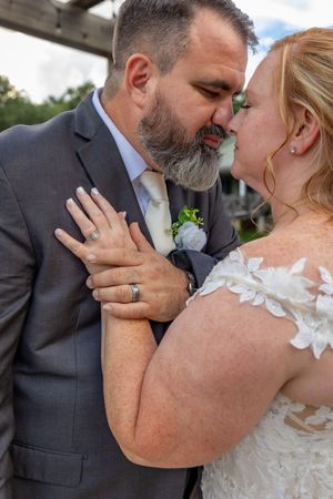 Bride and groom sharing a romantic kiss, groom in gray suit with boutonniere, bride in lace wedding dress.