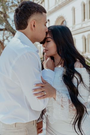 An intimate moment between a couple in formal wear, sharing a tender embrace against an architectural backdrop.