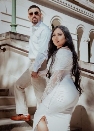 Stylish couple in all-white outfits pose on elegant stone steps during golden hour photoshoot.