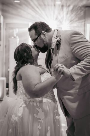 Black and white photo of a bride and groom sharing a romantic first dance kiss at their wedding reception.
