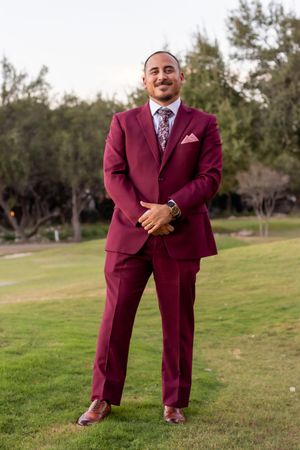 A person in a burgundy suit poses in different positions on a grassy field.
