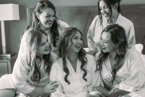 A group of people in white robes share joyful laughter while getting ready for a special occasion together.