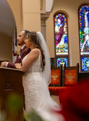 Stained glass windows cast colorful light inside a church sanctuary during a wedding ceremony.