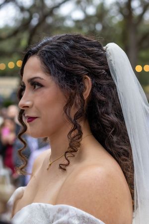 A side profile view of someone wearing a white wedding dress and veil with dark curly hair styled elegantly.
