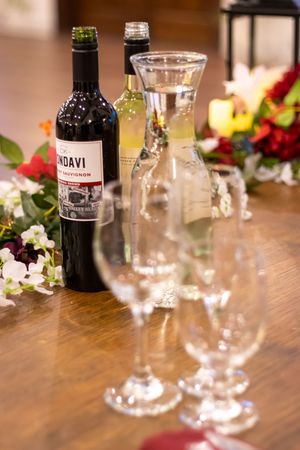 Wine bottle and empty glasses arranged on wooden table with floral decorations and water carafe.