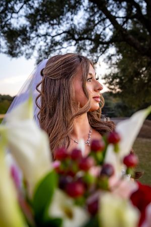 A dreamy bridal portrait in soft sunlight with blurred burgundy and white flowers in the foreground.
