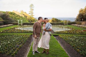 Mother and father kissing holding their toddler in a Newcastle NSW garden during a 1st birthday milestone photoshoot