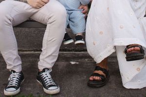 mum, dad, and toddler sitting on a bench, showing their shoes in a Newcastle NSW garden during a 1st birthday milestone photoshoot