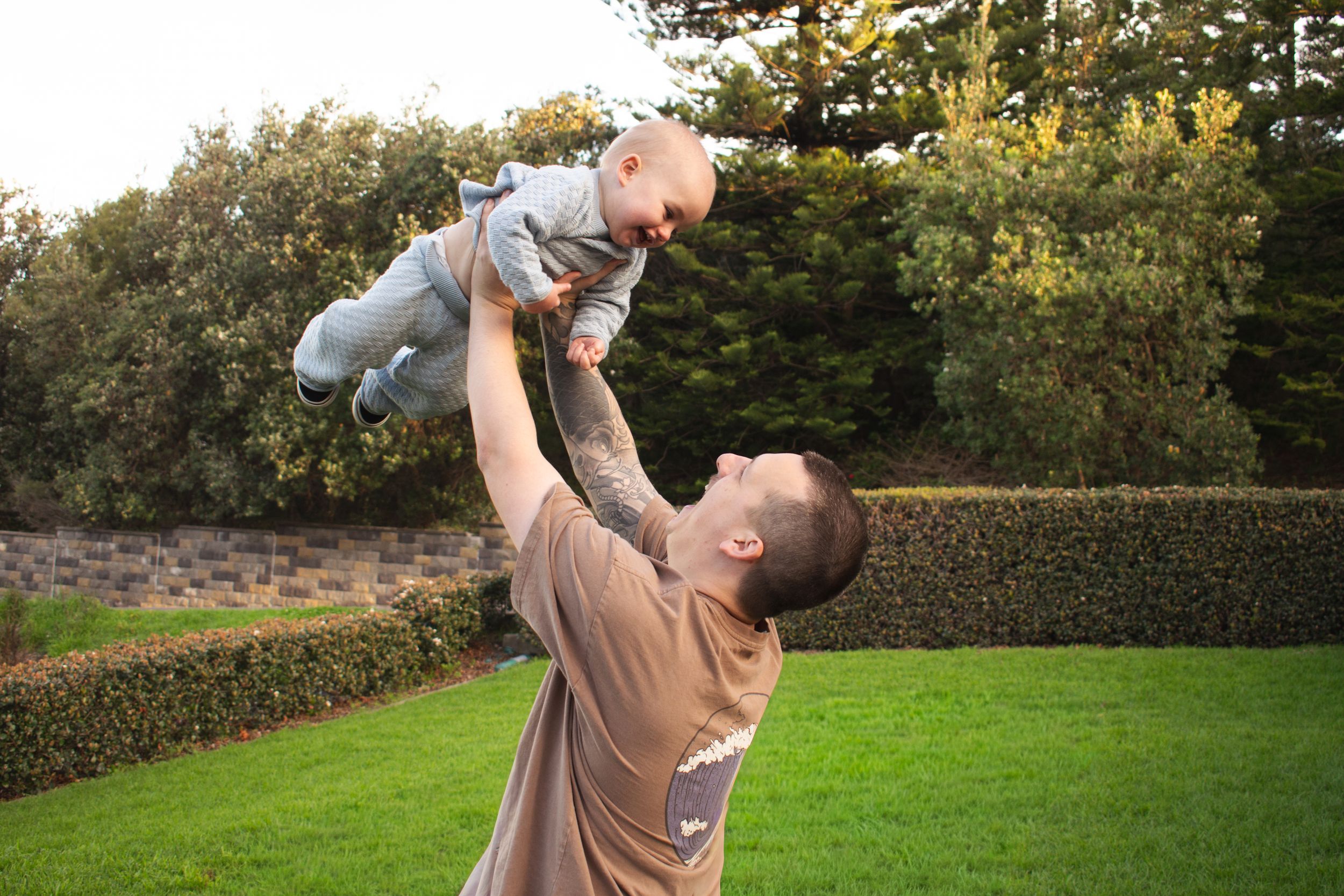 Dad throwing his toddler into the air in a Newcastle garden during a 1st birthday milestone photoshoot
