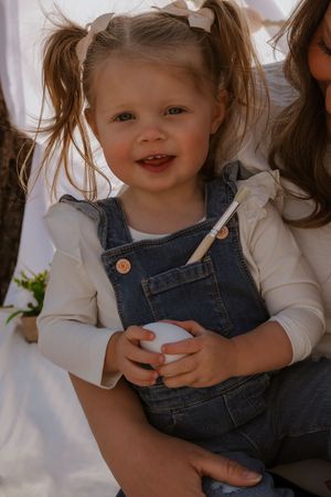 Candid moment showing denim overalls and white sweater in natural light.