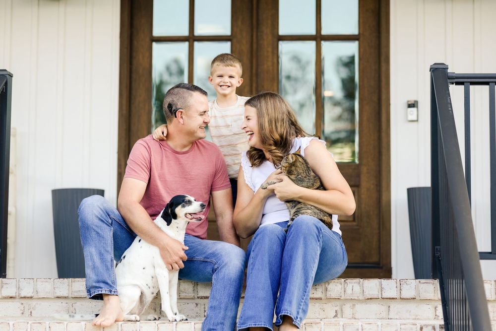 A couple sits together on a porch step with their small white dog, sharing joyful moments outdoors.