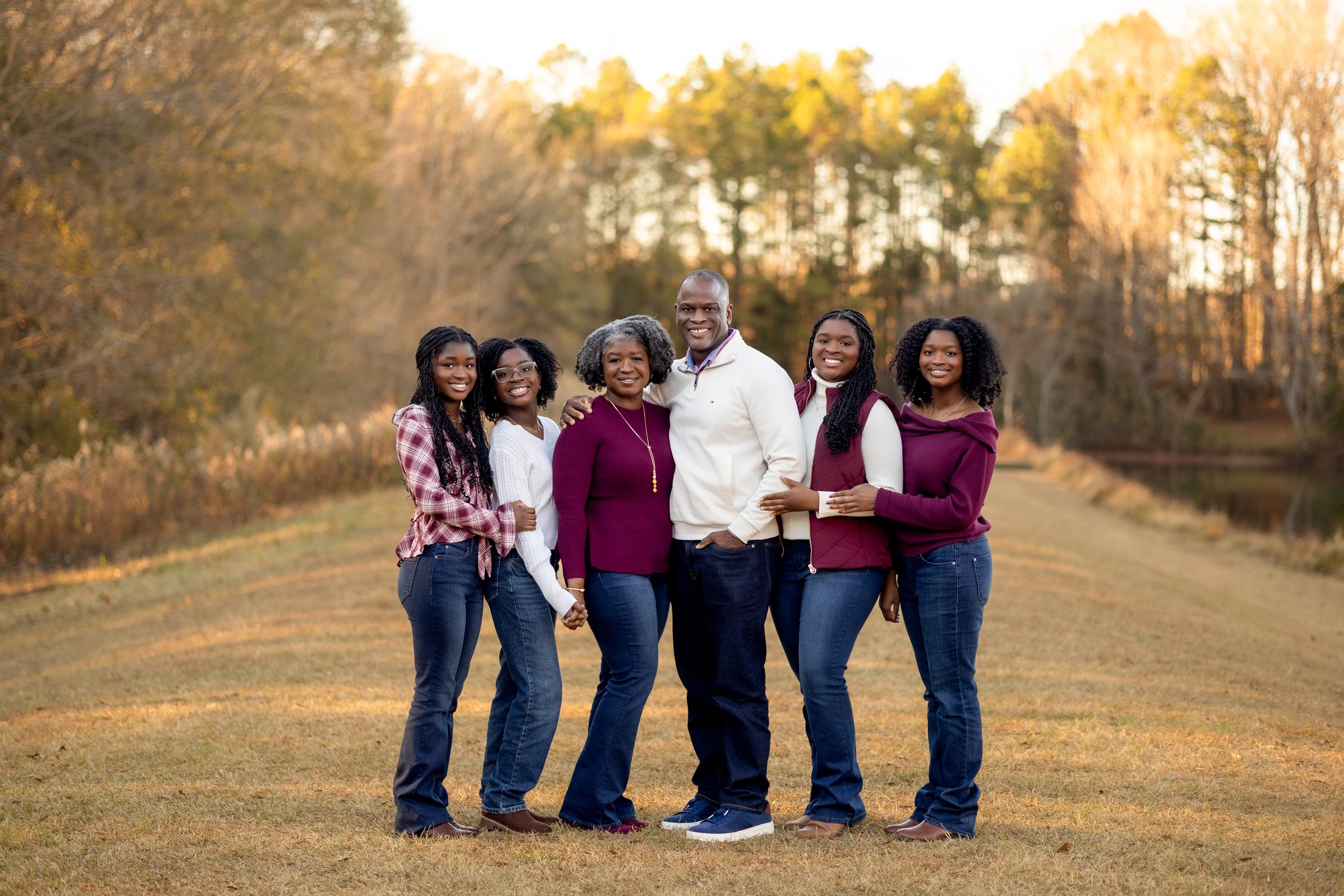 A group of people in coordinating outfits pose together on a rustic autumn path at sunset.
