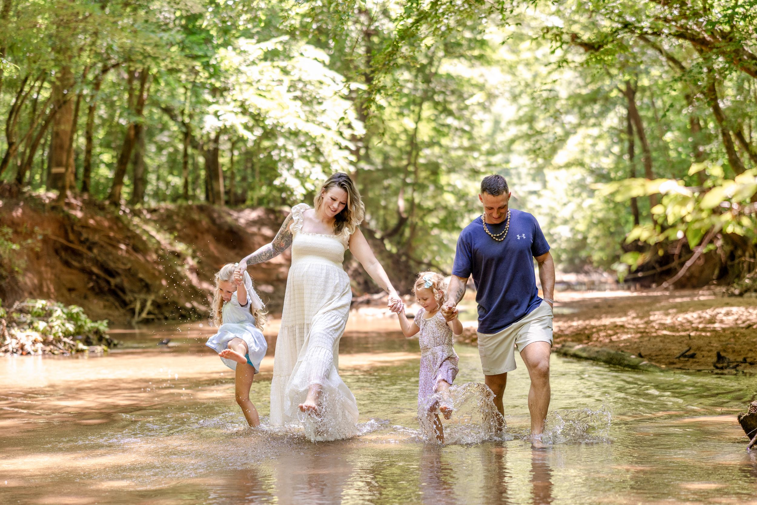 Family enjoying a fun photo session in a sunlit forest creek, splashing and playing in the shallow water.