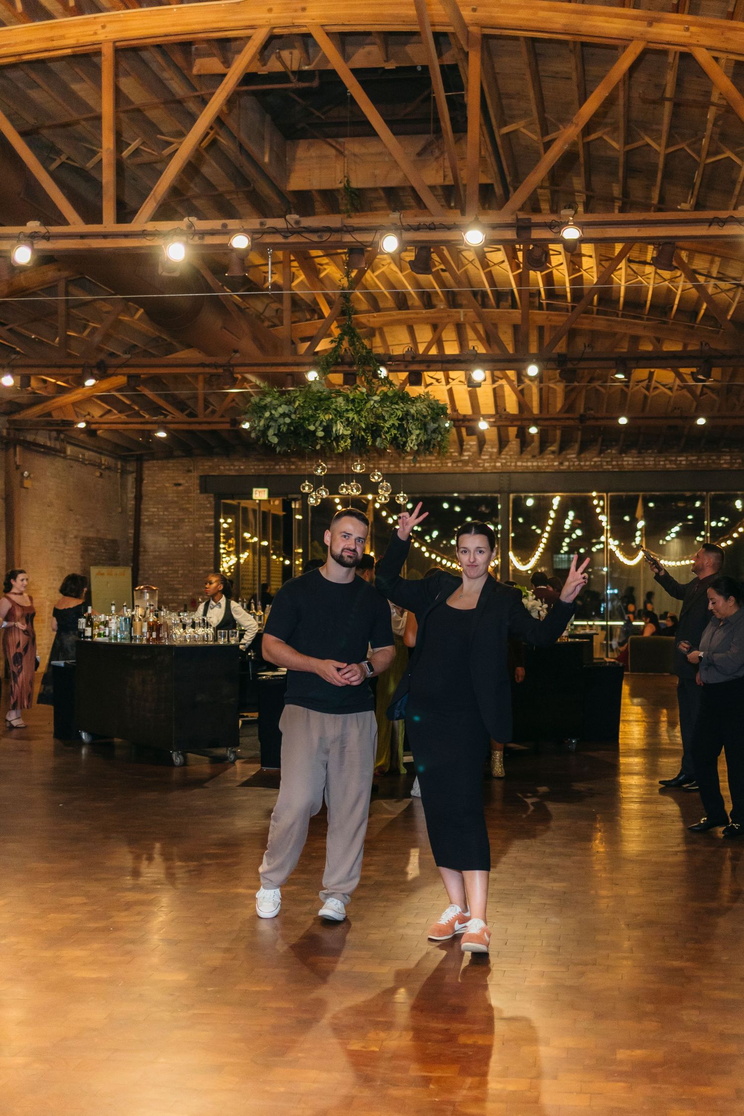 Chicago wedding photographer and videographer work in a spacious venue with exposed wooden beams and twinkling lights overhead.