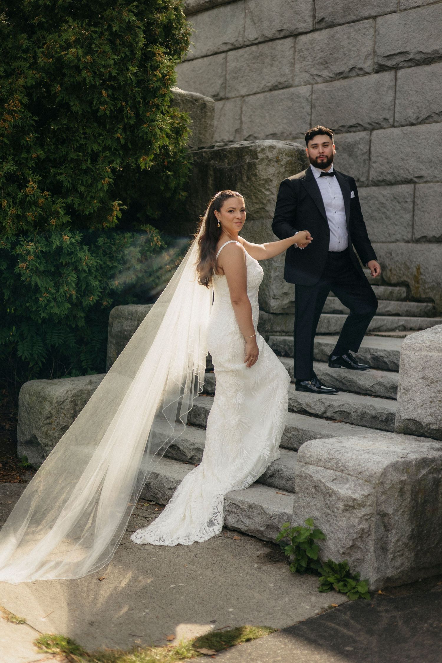 Chicago Wedding couple poses on stone steps with flowing white veil creating candid romantic outdoor portraits.