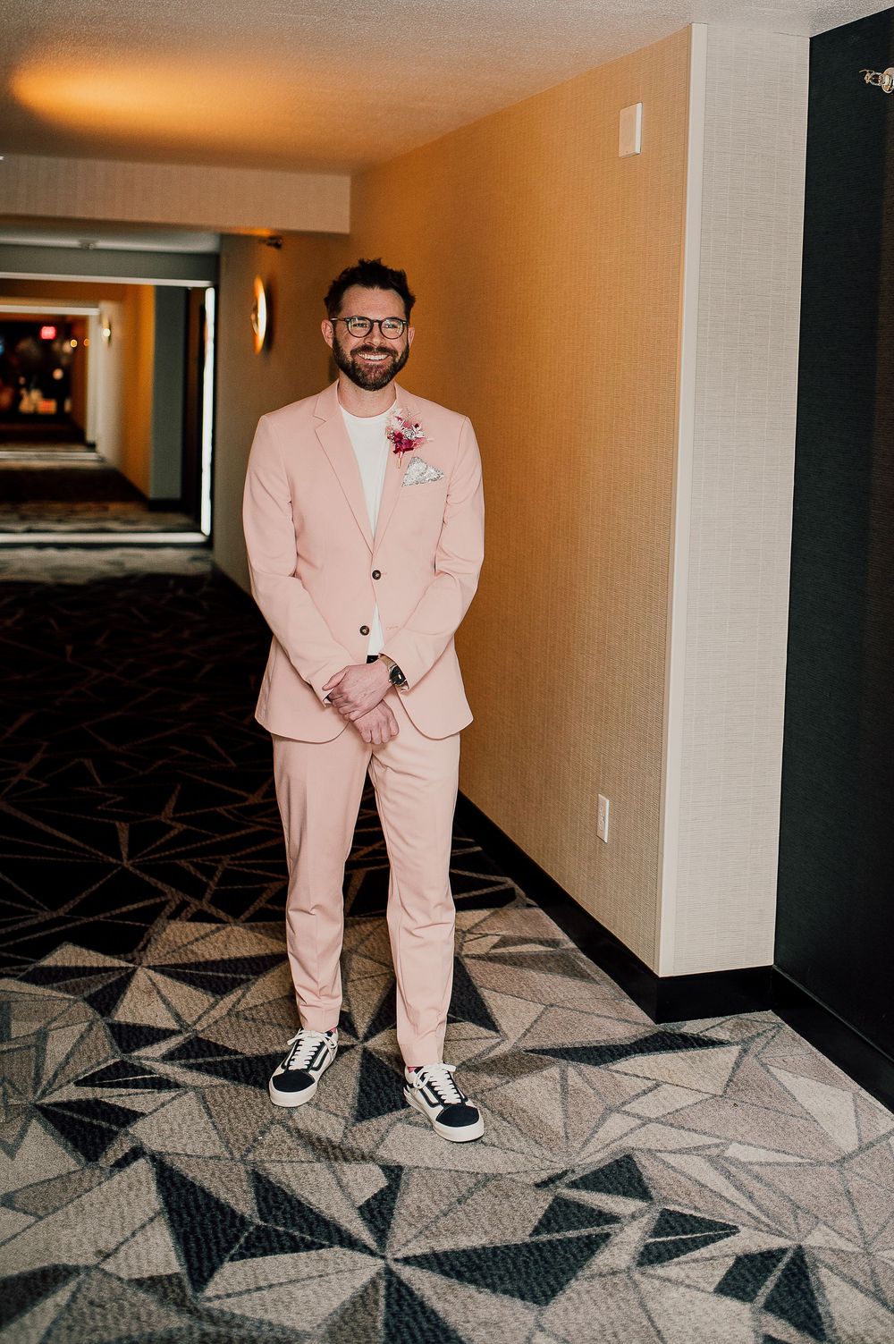 Four sequential photos showing someone in a pink suit and sneakers posing in a hotel hallway with geometric carpet pattern.