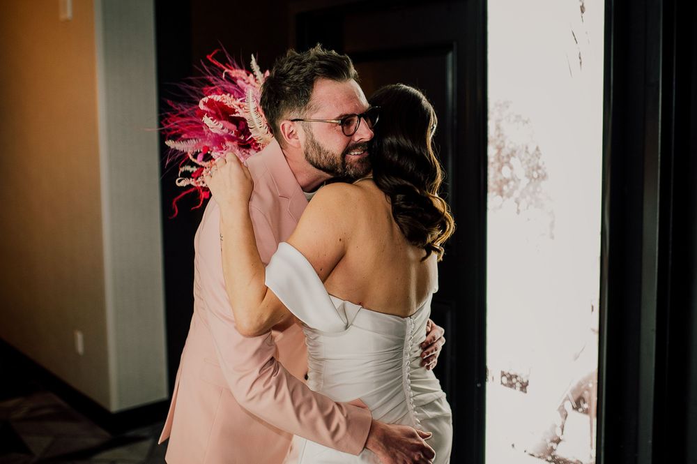 A couple shares a romantic embrace in a hallway, with the bride wearing a white strapless gown.
