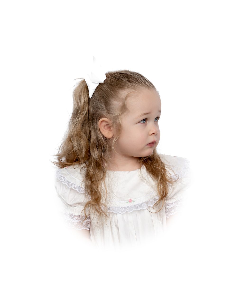 Young child in a white dress with blonde hair and a white bow gazes to the side in a portrait style photo.