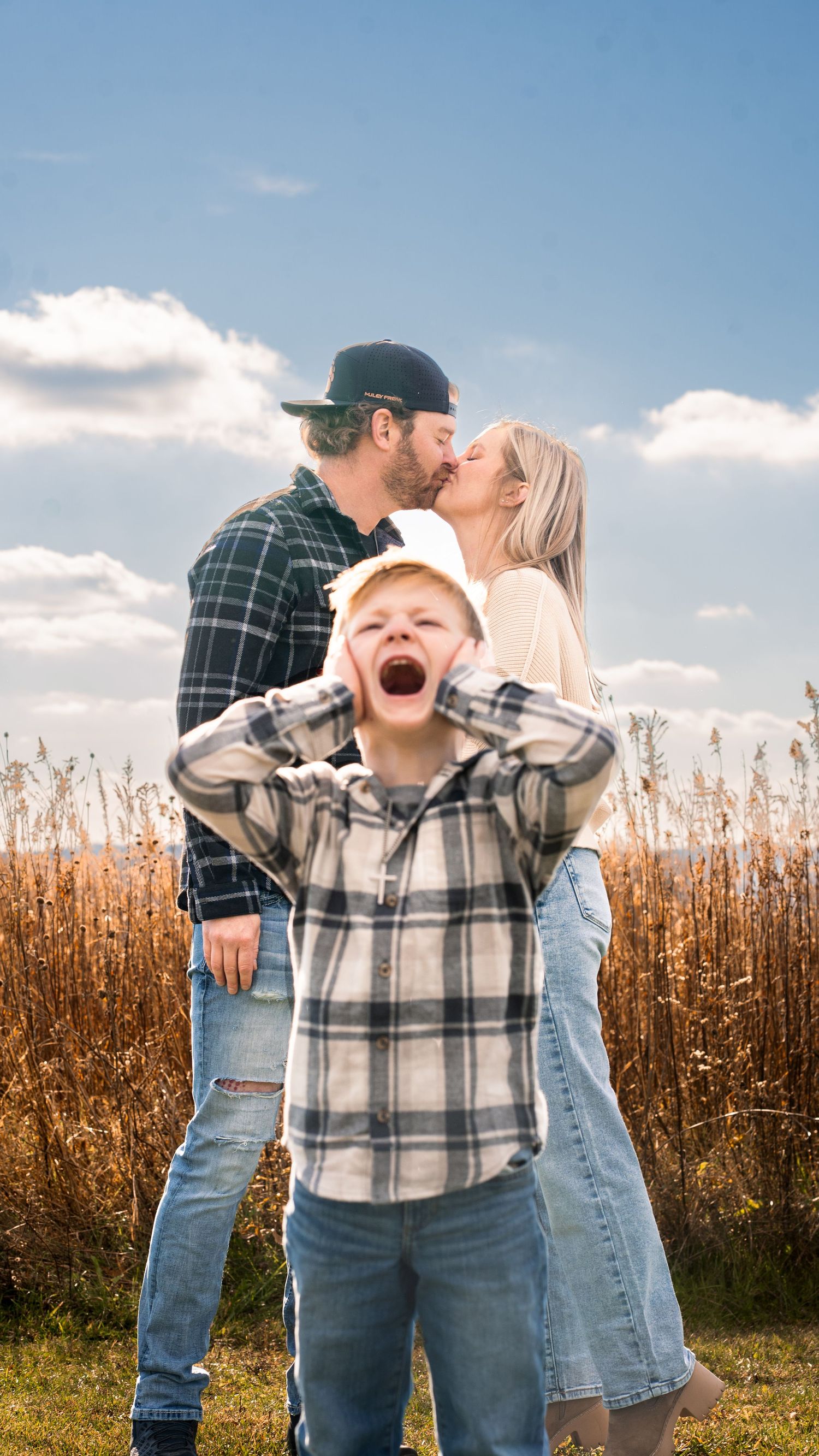 Family wearing plaid and denim shares joyful candid moments together in a golden cornfield at sunset.