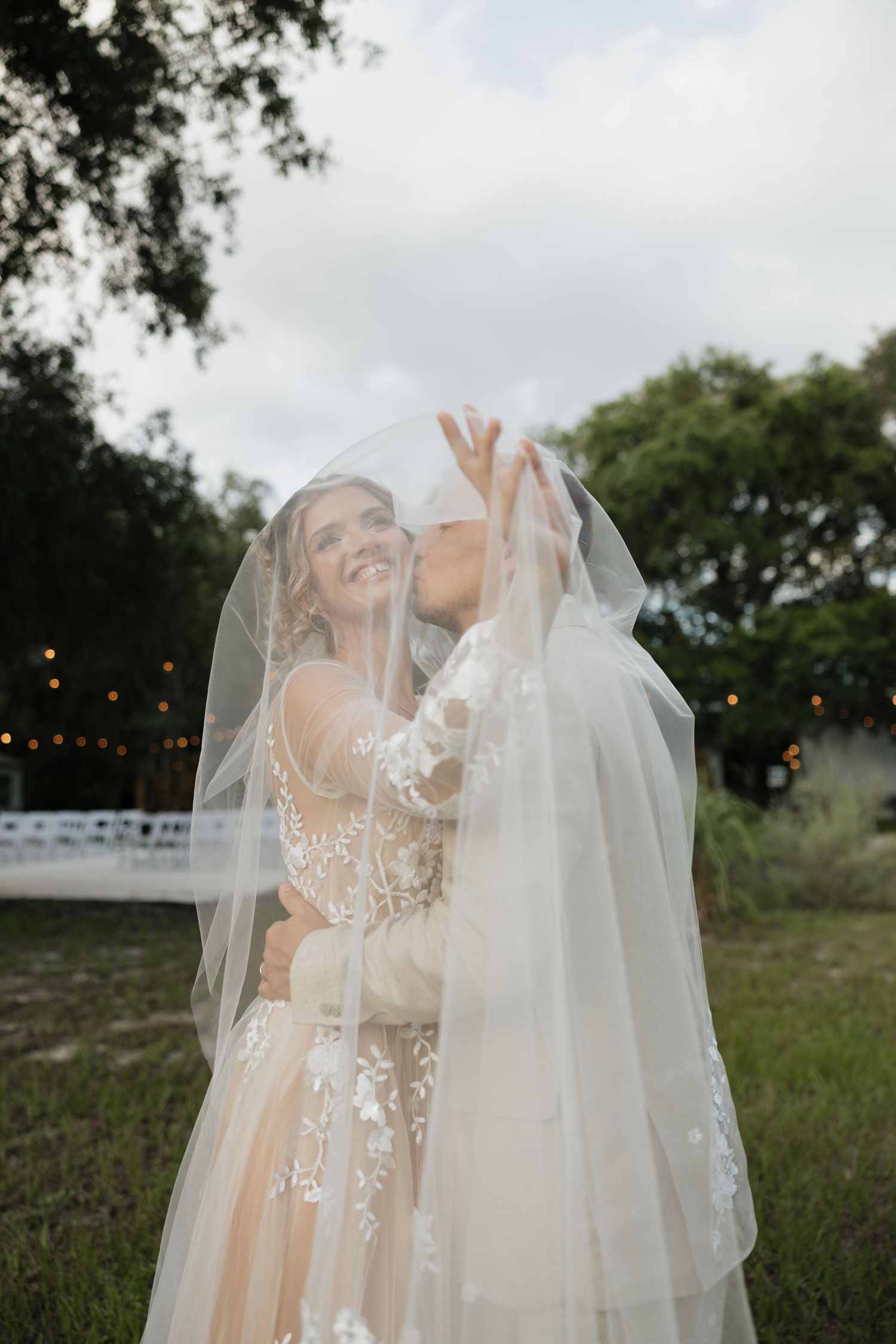 Wedding dress and veil detail shots on wooden church pews surrounded by trees.