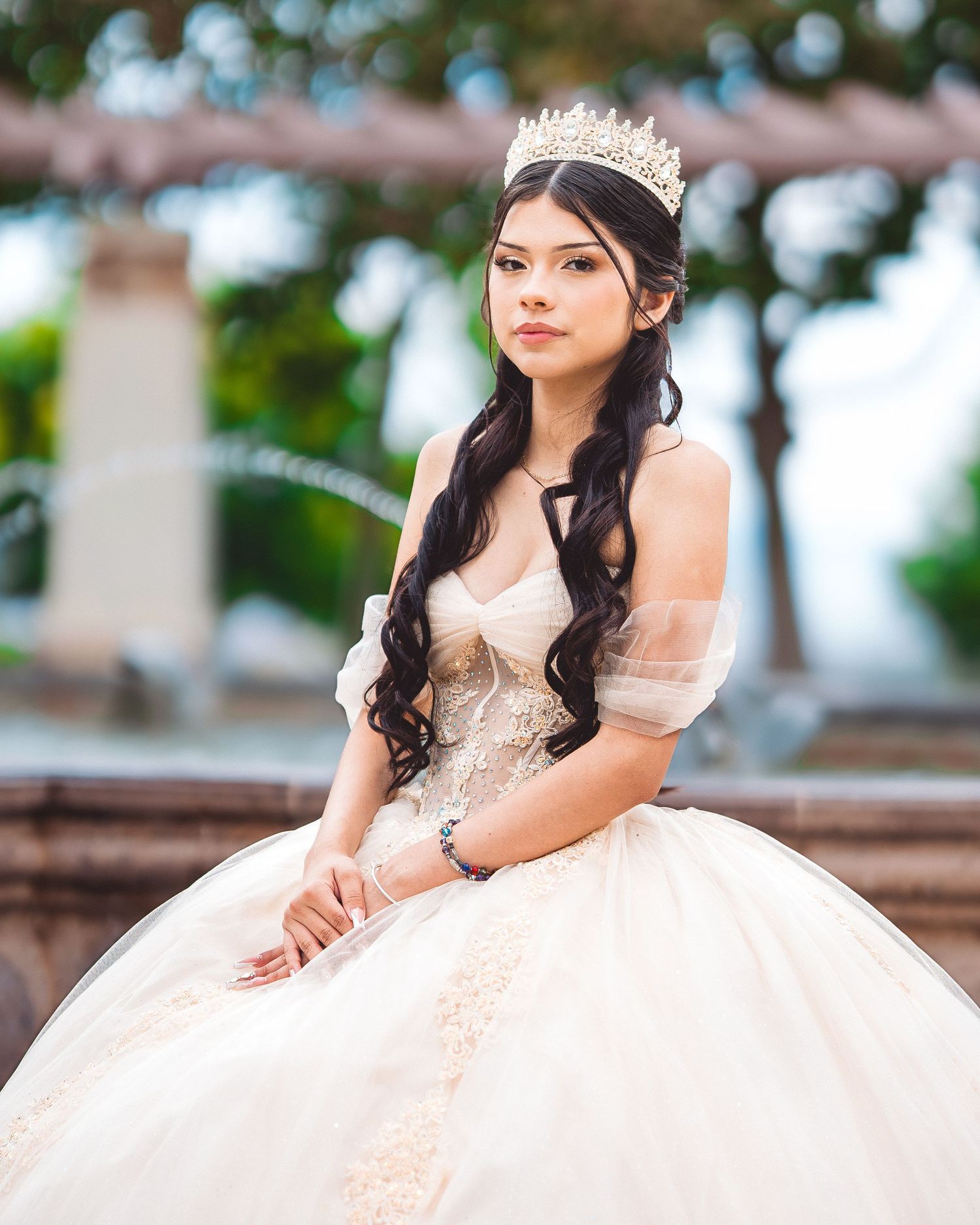 A person in an elegant blush pink quinceañera gown with embellishments poses outdoors for formal portraits.