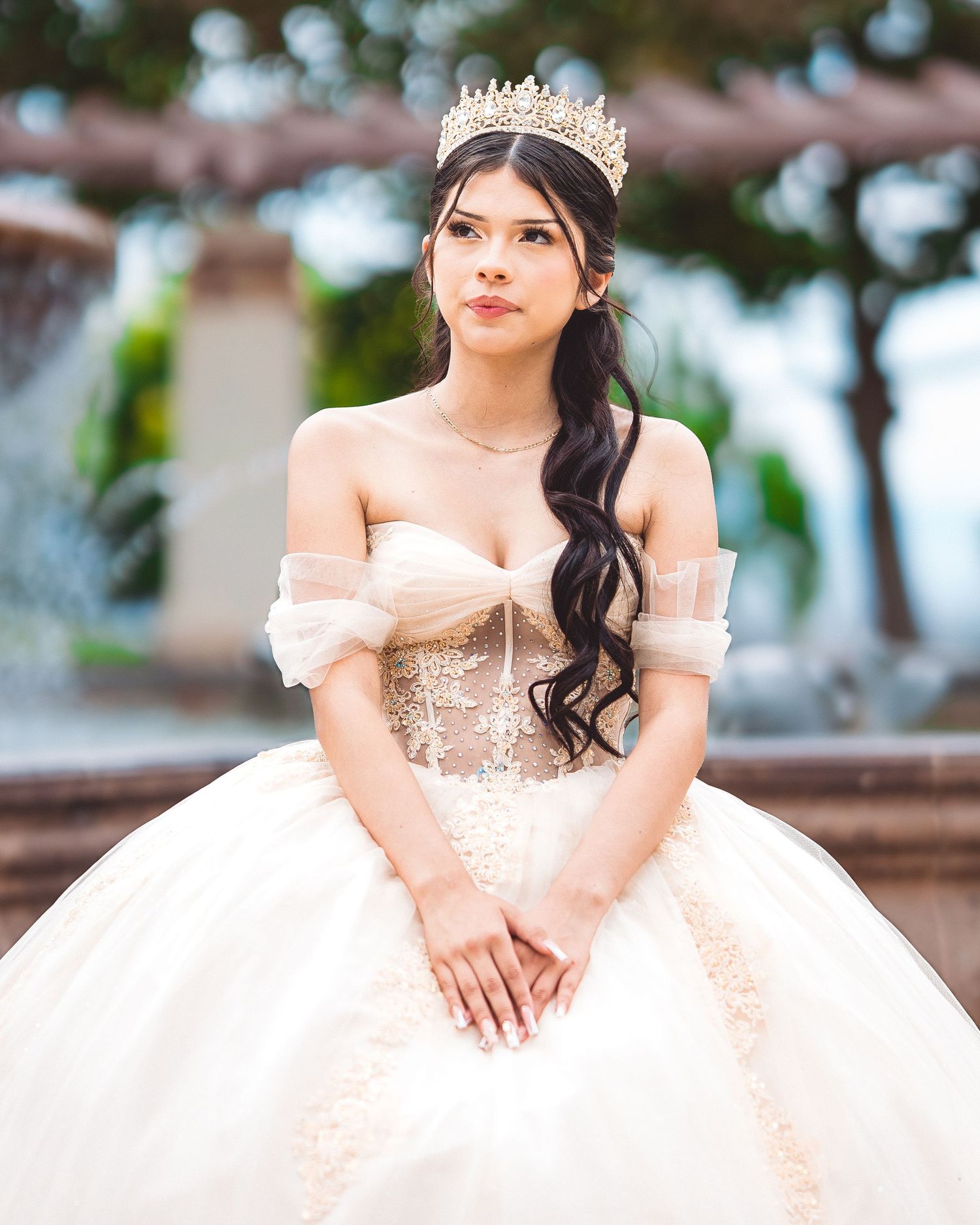 A person in a blush pink ball gown and tiara poses outdoors for a formal portrait session.