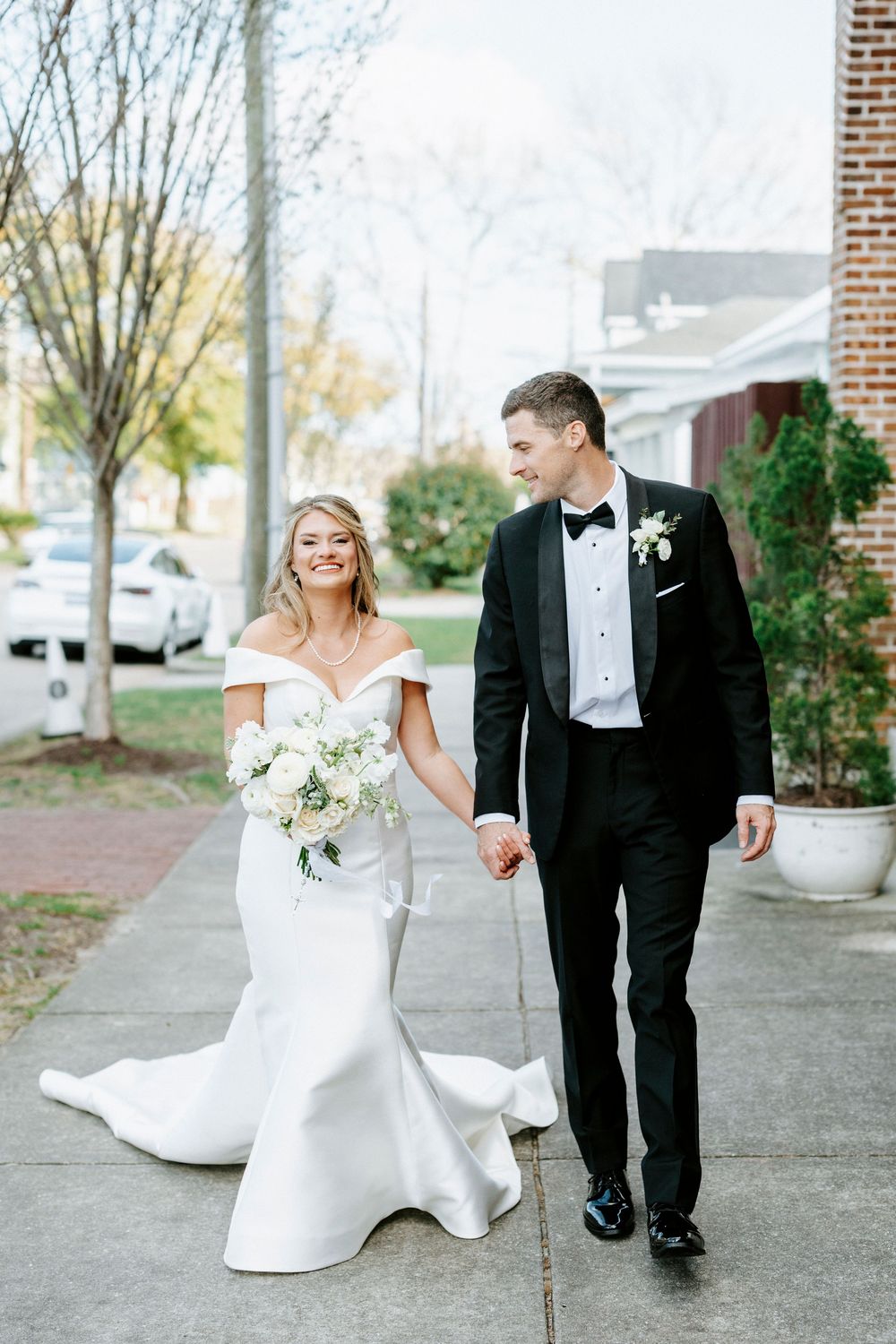 Couple in formal wedding attire walking and laughing together on outdoor path.