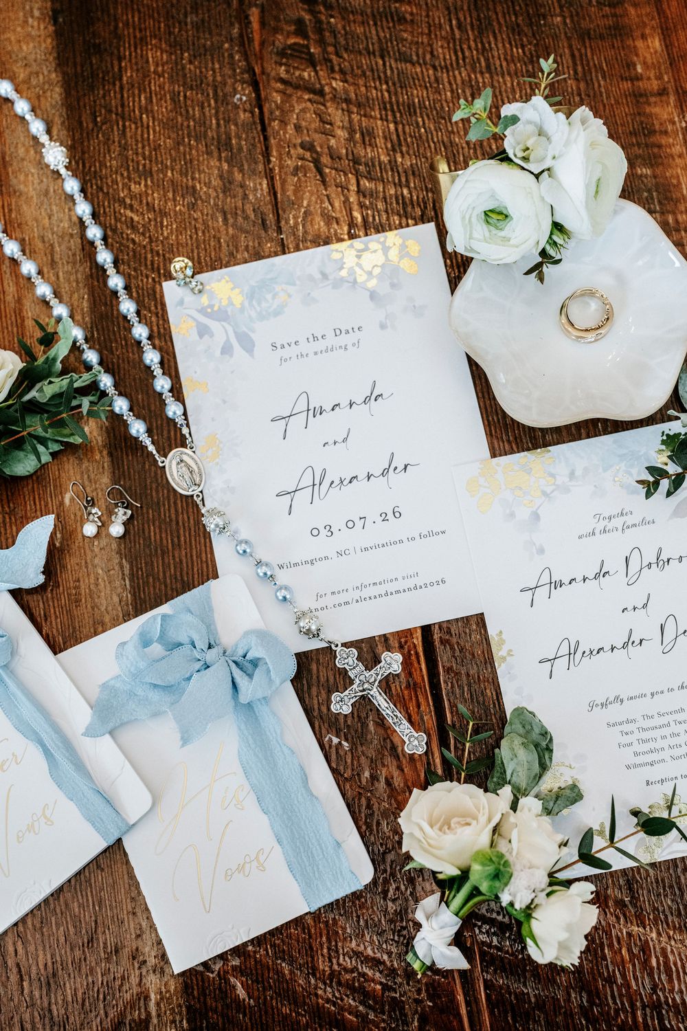 Elegant wedding invitation suite with white flowers and blue accents on rustic wooden background.