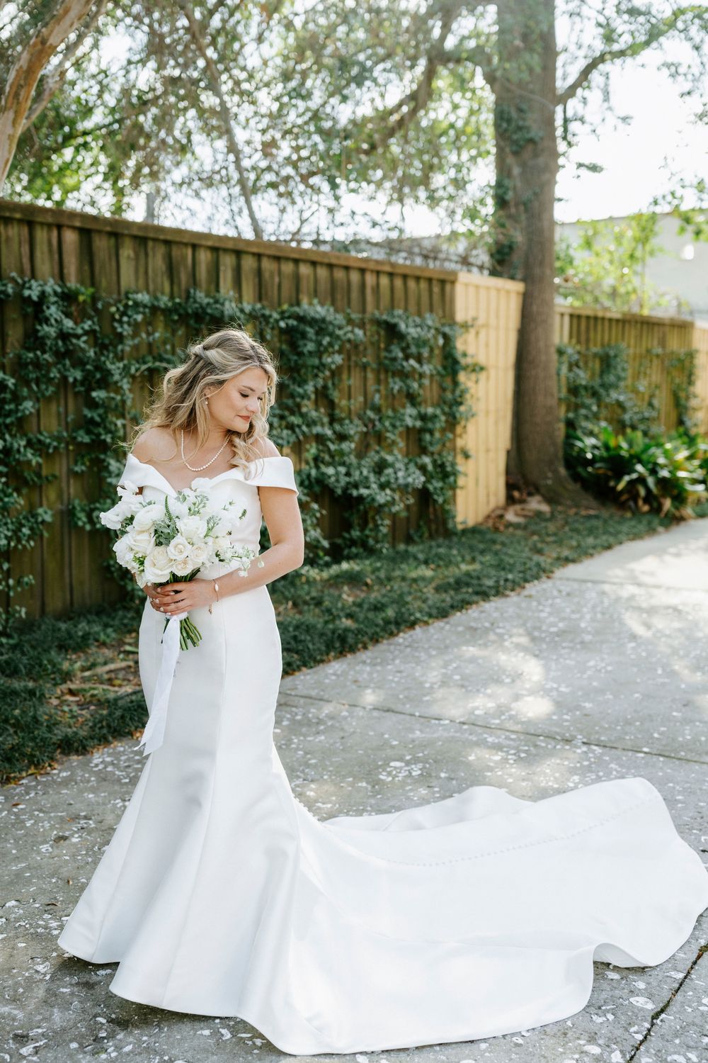 A bride in an elegant off-shoulder white wedding gown twirls joyfully in a garden setting with flowing dress movement.