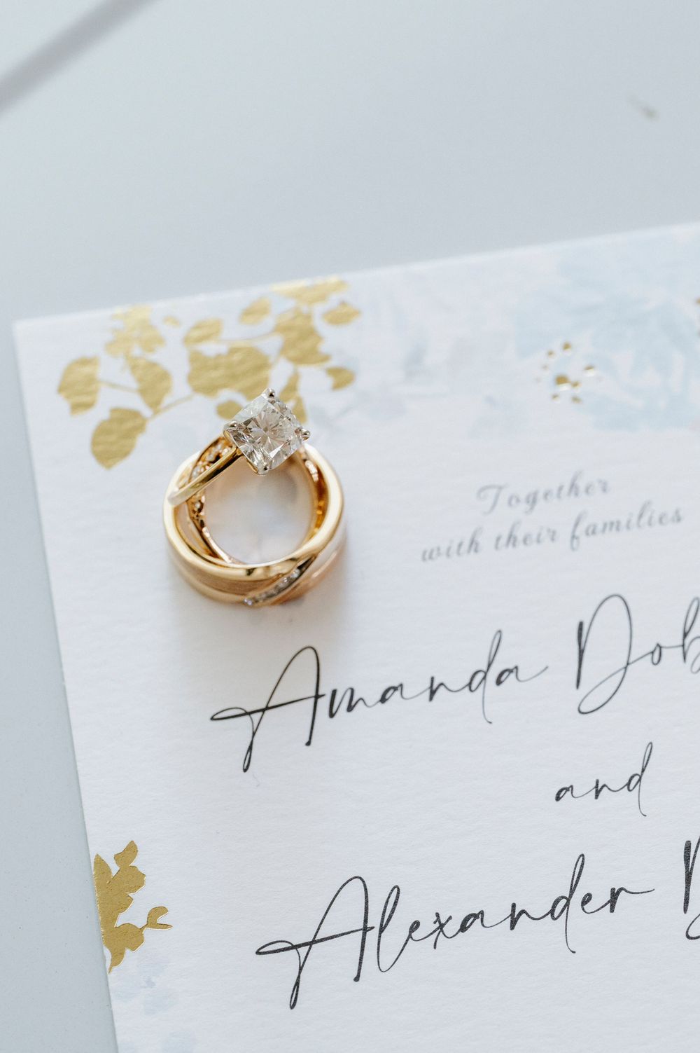 Gold wedding rings photographed on an elegant wedding invitation with gold foil details.