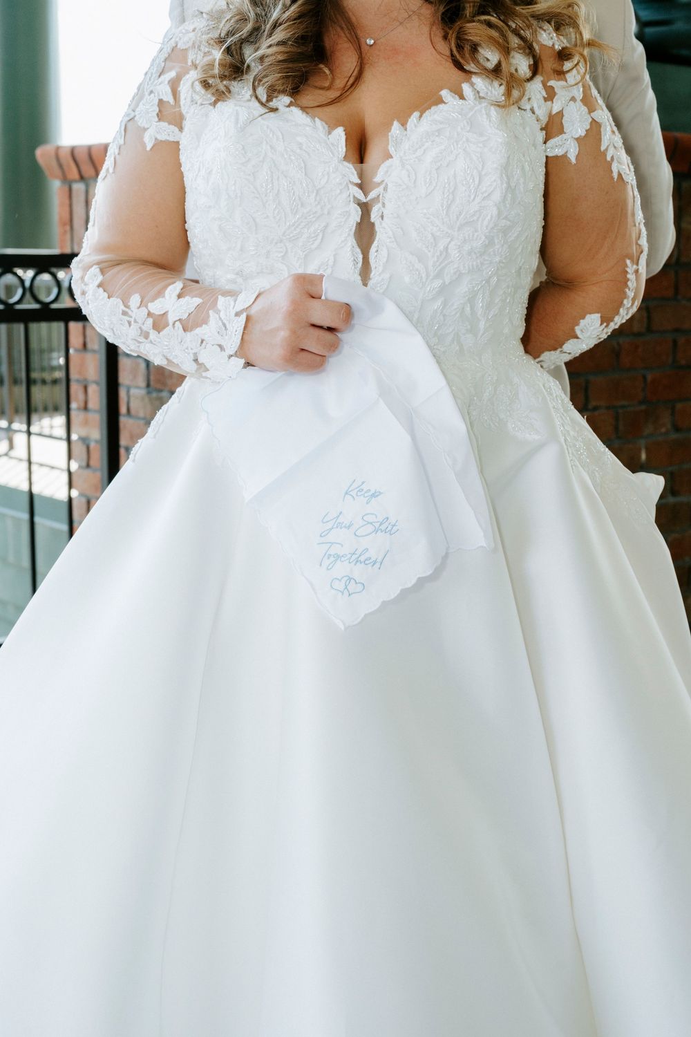 Close-up detail of a white lace wedding dress with sheer sleeves and an embroidered handkerchief.