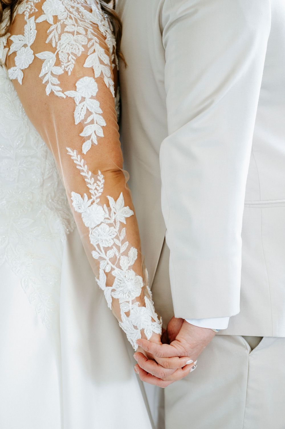 Close-up details of white lace sleeves against a light background showing intricate floral patterns.