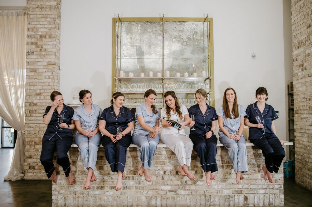A panoramic view of a wedding party leaning against a rustic brick wall in coordinated formal attire.