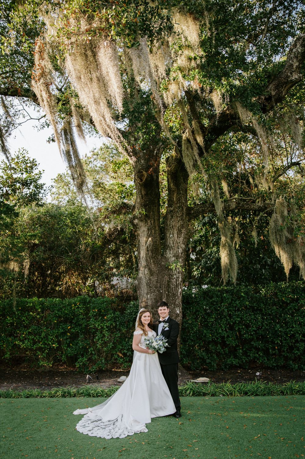 Romantic outdoor wedding portraits under Spanish moss draped trees with lush green hedge backdrop.