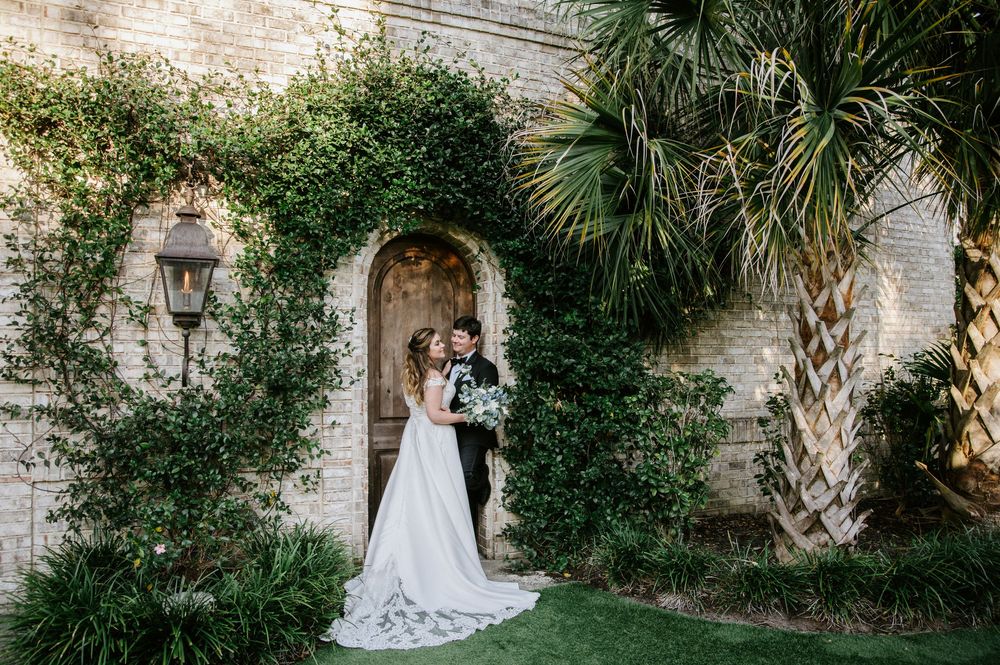 A romantic scene in a garden courtyard with stone walls, climbing vines, and a palm tree framing an arched doorway.