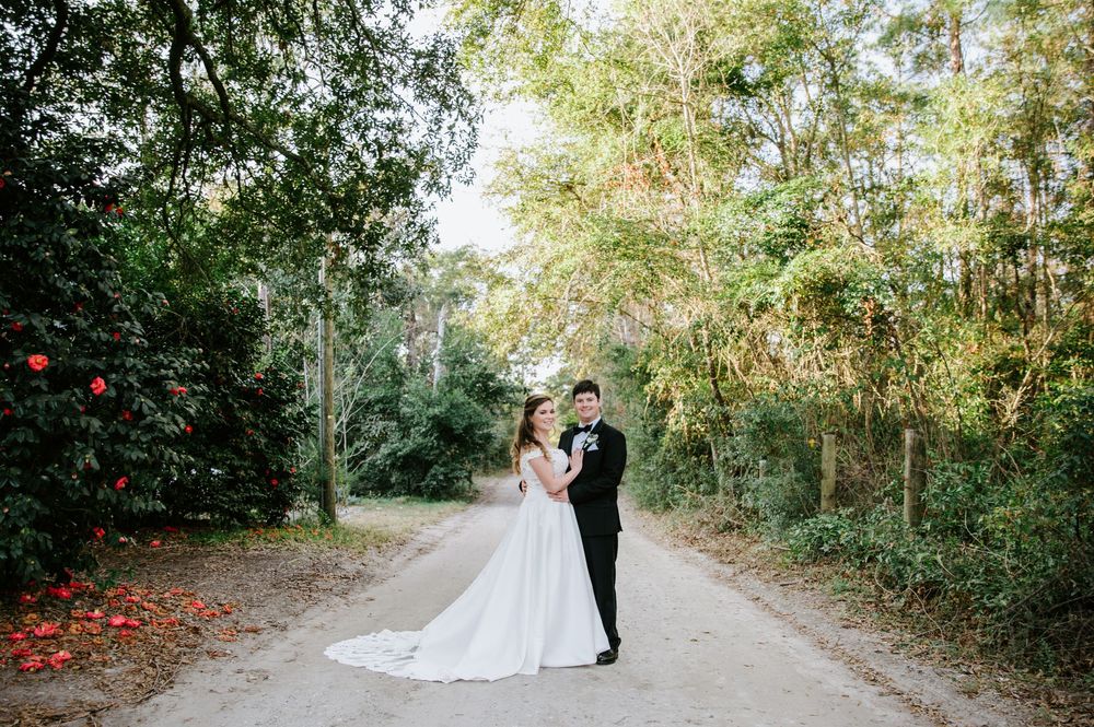 A couple in wedding attire stands together on a tree-lined path during an outdoor autumn ceremony.