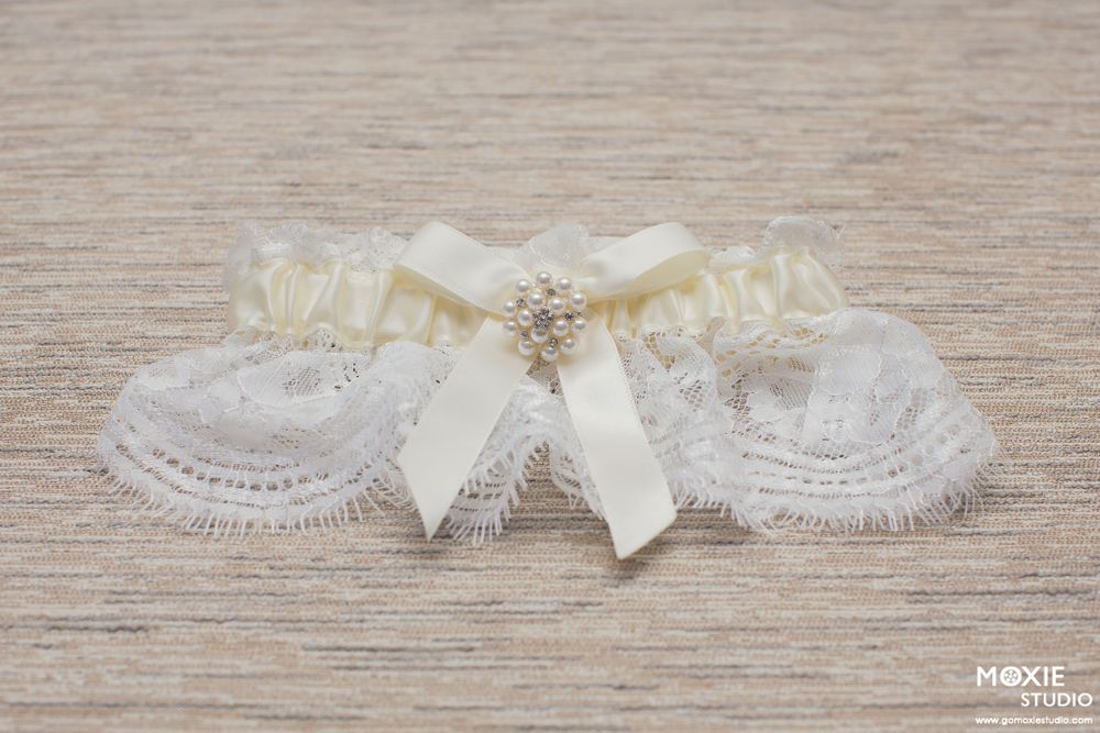 Delicate ivory lace wedding garter with cream bow and crystal embellishment on wooden surface.