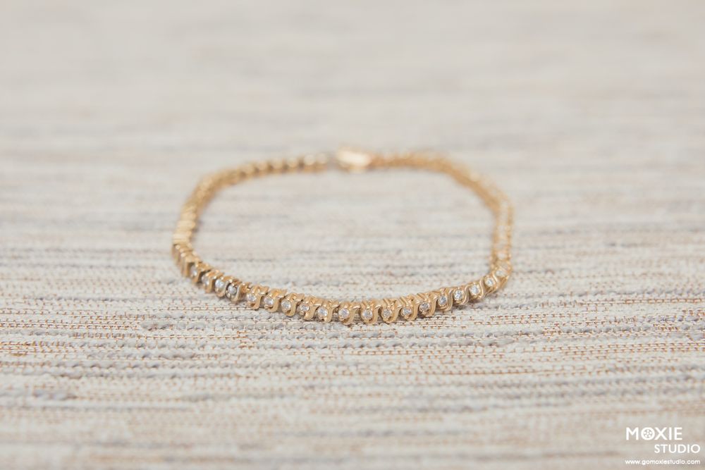 Delicate gold beaded bracelet displayed on a light beige linen textured background.