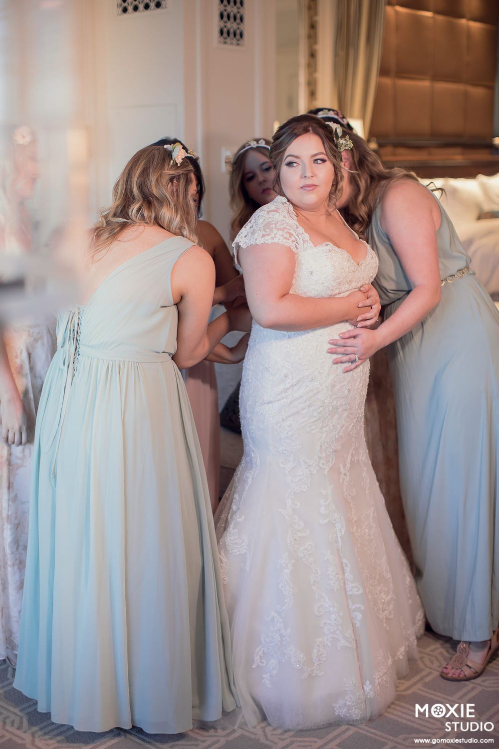 Wedding party members in mint green bridesmaid dresses and white bridal gown pose together at elegant indoor venue.
