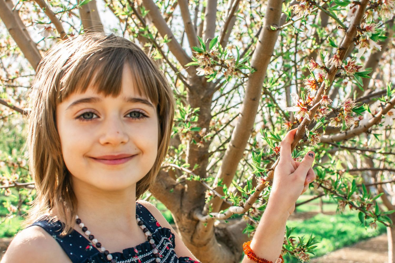 A series of four photos showing a child smiling under pink spring blossoms in a garden setting.