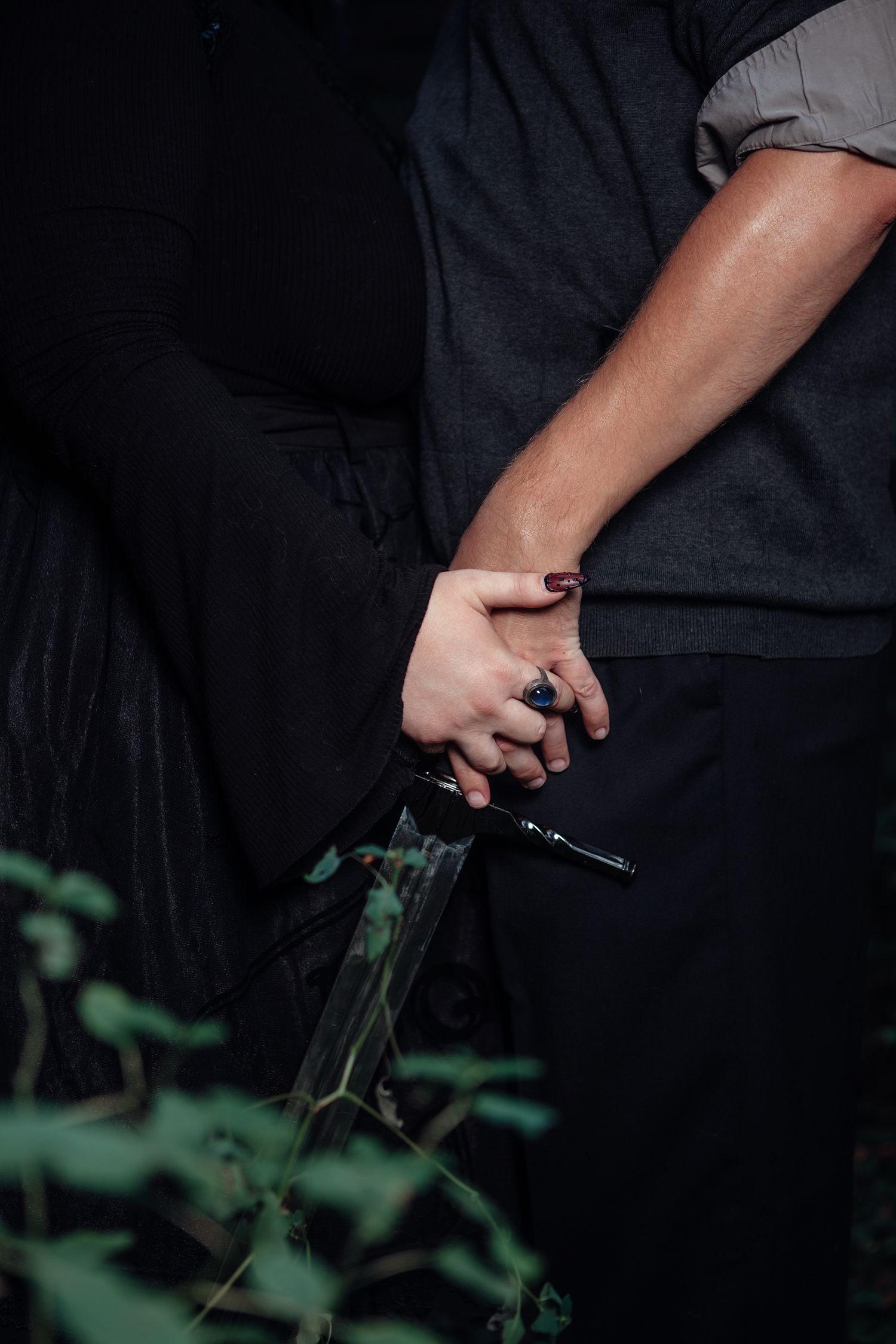 A hand holds a black pistol against a dark background with green foliage visible at the bottom of the frame.