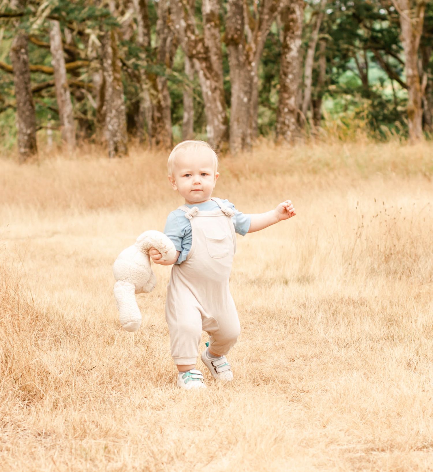 Small child in denim overalls running and playing in a golden field of tall grass during autumn.