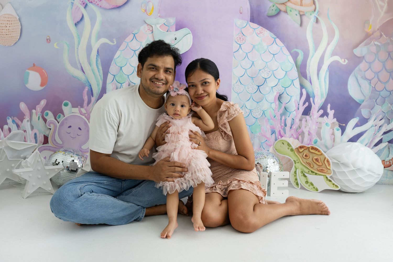 Family poses together against whimsical underwater themed backdrop with pastel colors and decorative elements.
